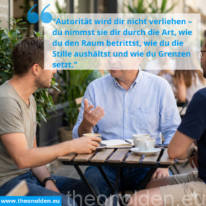 Älterer Berater mit Brille erklärt einem jüngeren Mann an einem Cafétisch im Freien das Thema 'Status-Spiele in der Beratung'. Die Atmosphäre ist entspannt bei Kaffee.