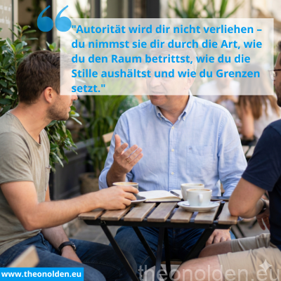 Älterer Berater mit Brille erklärt einem jüngeren Mann an einem Cafétisch im Freien das Thema 'Status-Spiele in der Beratung'. Die Atmosphäre ist entspannt bei Kaffee.